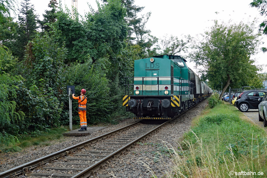 Wegen fehlender-fahrzeuggerechte n Einschalttechnik, müssen die Bedienfahrten stehts vor den technisch gesicherten Bahnüberghängen anhalten. Am 18.08.2024 hat Lok V140 mit dem Leergetreidezug aus Zörbig gehalten. Der Lokführer sichert manuell den Bahnübergang in der Straße der Neuen Zeit in Sandersdorf.