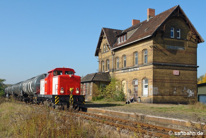 Die frisch Hauptuntersuchte V60-Lok 345 229-9 der Regiobahn Bitterfeld befindet sich am 13.10.2008 mit ihrem Ethanolkurzzug aus Zörbig gerade auf Durchfahrt in Sandersdorf, als sie vor der damals noch unbewohnten, unsanierten Gebäudessilhouette des gleichnamigen Ortes vorüber fuhr. 