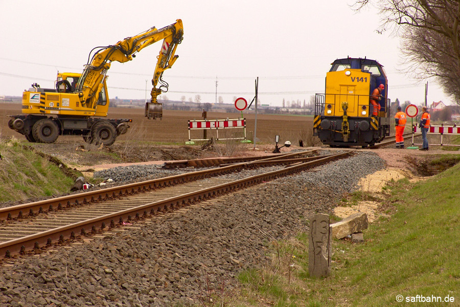 Bahnbetrieb auf der Saftbahn im Jahr 2006: Laufende Gleisbauarbeiten mussten hin und wieder unterbrochen werden, um die Bedienung des Anschlussgleises der heutigen Verbio SE zu ermöglichen. V141 gelangte am 10.04.2006 nach Zörbig, um eine Kesselwagengruppe abzuholen. Zuvor musste der Zweiwegebagger ausgleisen, um Platz für die Lokdurchfahrt zu machen. 